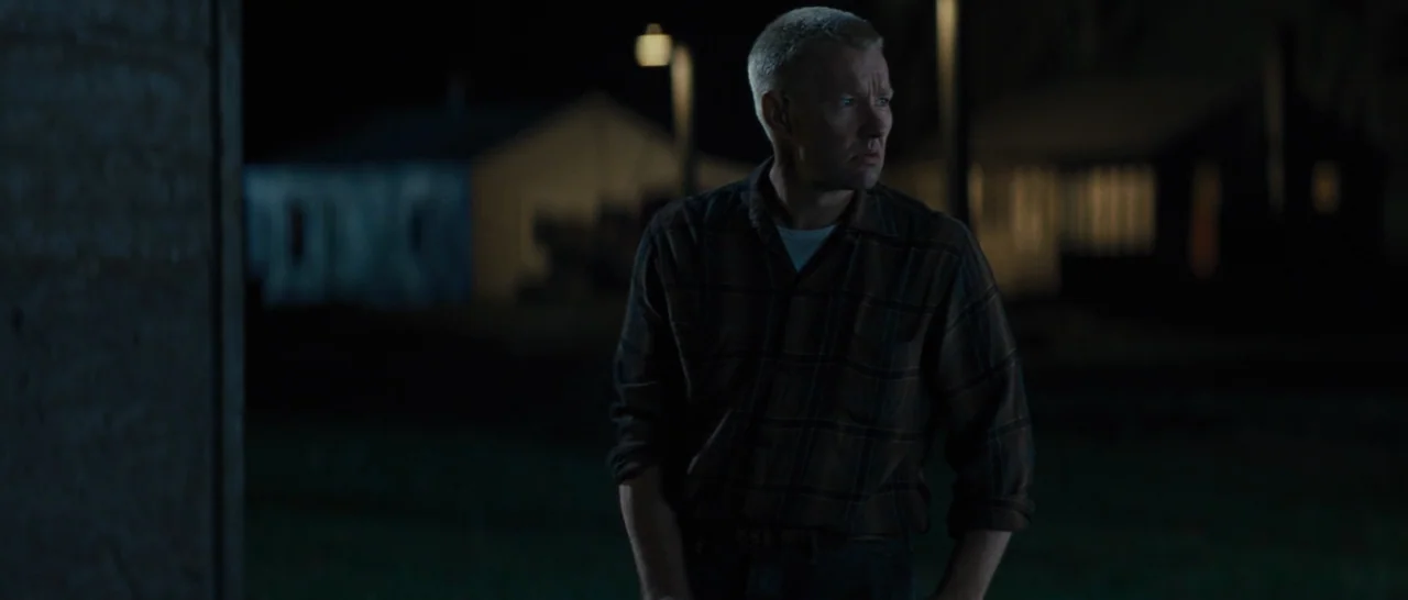 Loving (2016) movie still: medium — A man stands outdoors at night near a dimly lit building with muted lighting. The subject looks towards the…