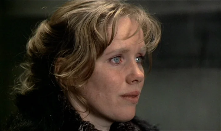 The Serpent’s Egg (1977) movie still: closeup — A dimly lit indoor space with a neutral, slightly blurred background. A woman with blonde hair looks…
