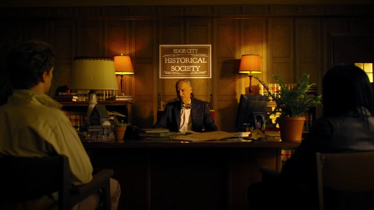 Suburban Gothic (2014) movie still: medium — An office with wood-paneled walls features a sign reading Edge City Historical Society. An elderly man…