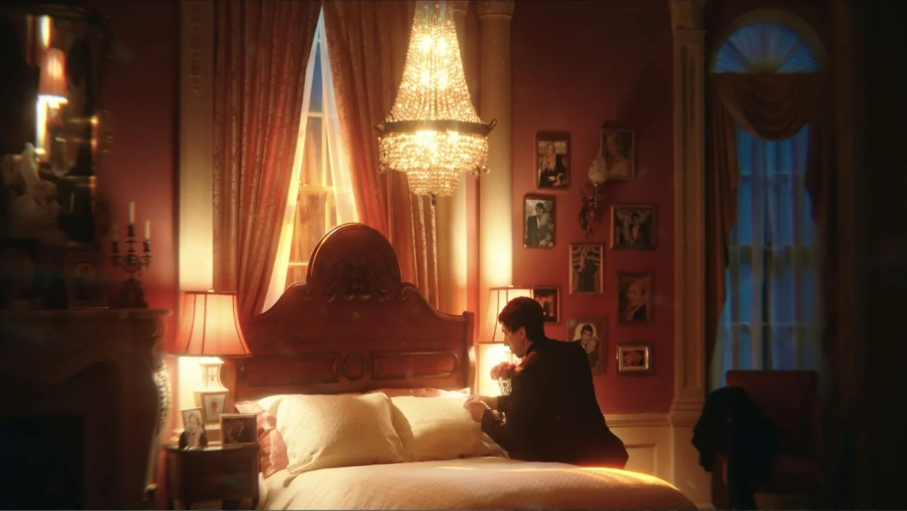 Megalopolis (2024) movie still: medium — A vintage style bedroom features deep red walls adorned with many framed photographs. A man in a dark suit…