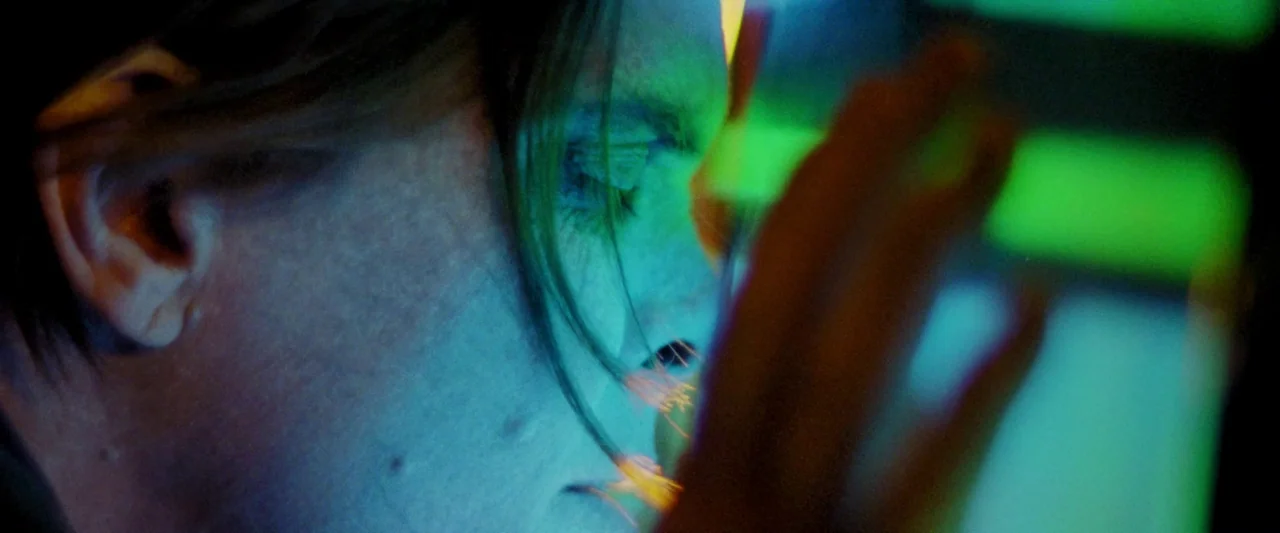 Moon Garden (2022) movie still: closeup — A person's face is illuminated by the intense green and blue light of a screen. The subject stands close…