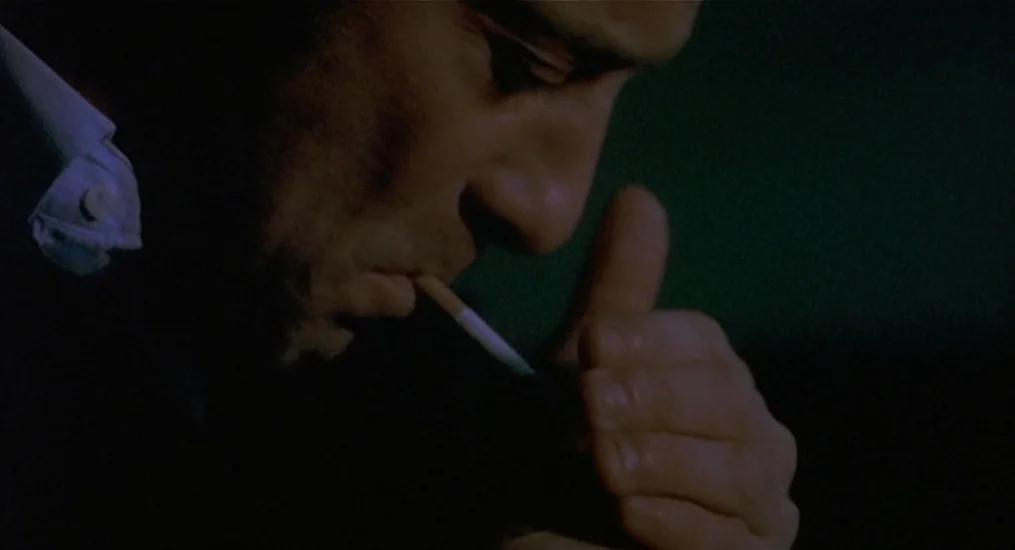 Vendredi Soir (2002) movie still: closeup — A man stands in a dark environment with only his face visible. He is lighting a cigarette with a small,…