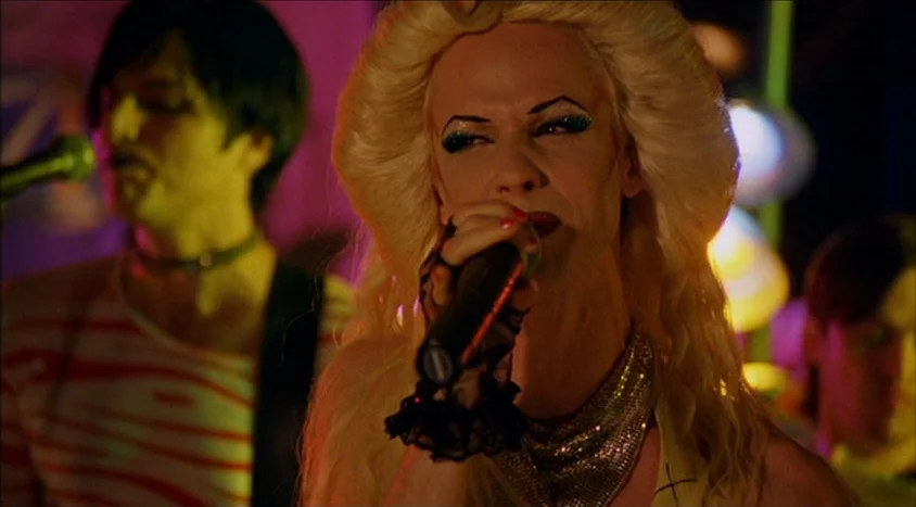 Hedwig and the Angry Inch (2001) movie still: medium — A dimly lit musical environment features a singer on a small performance area. The blonde…
