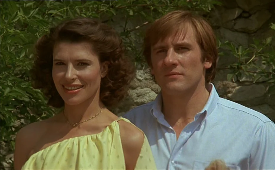The Woman Next Door (1981) movie still: medium — An outdoor area with a rustic stone wall and green leafy plants in background. A woman in a yellow…