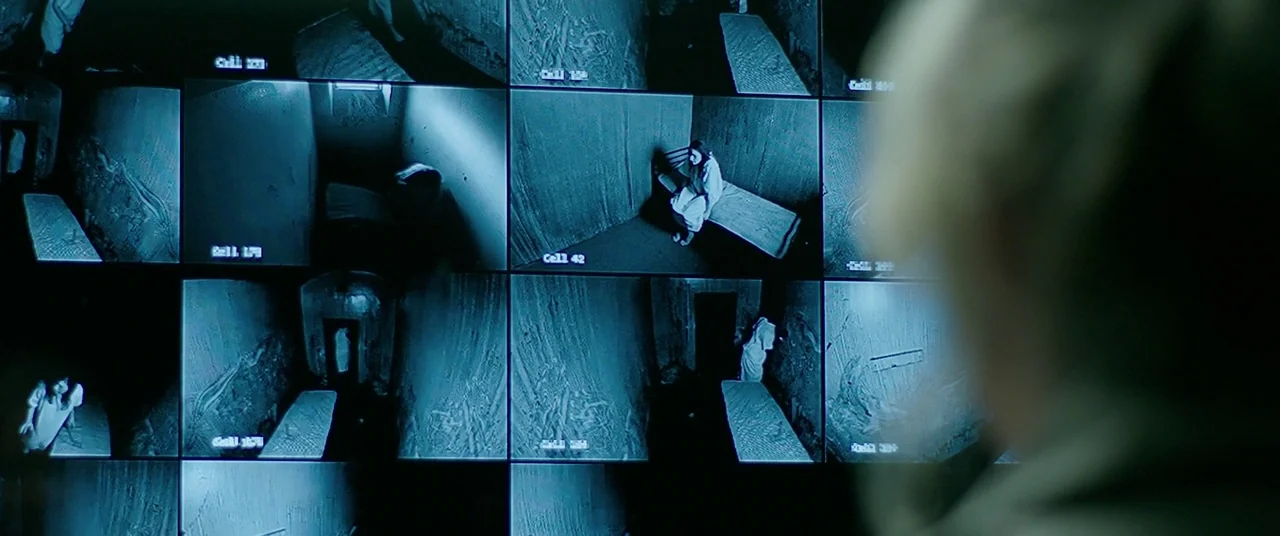 The Cured (2017) movie still: medium — A dark security room features a large wall monitor displaying multiple live video feeds. Each frame shows a…