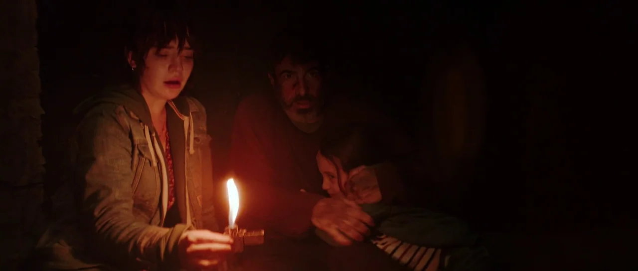 The Boogeyman (2023) movie still: medium — A dark, unadorned room provides the setting for three people huddled together closely. A young woman…