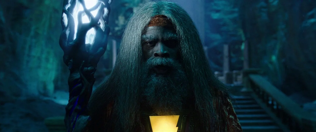 Shazam! (2019) movie still: medium — A dark stone interior features carved steps in the background and misty atmosphere. A long-haired elderly man…