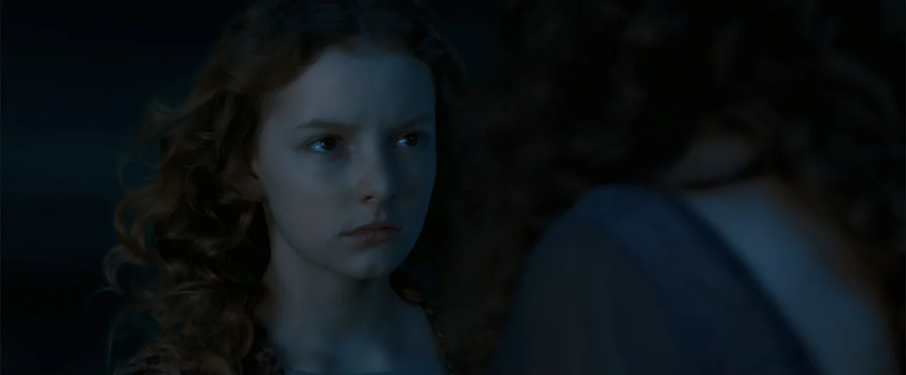 The Golden Compass (2007) movie still: closeup — A dark outdoor space features a young girl in the foreground against a blurred companion. The girl…