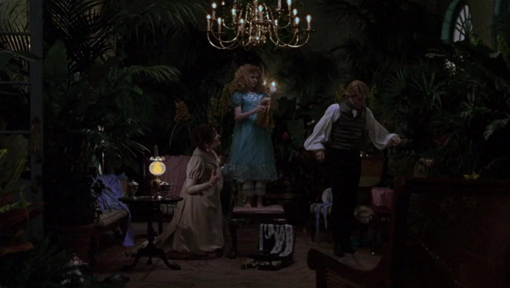 Interview With The Vampire movie still: wide — A dark, plant-filled greenhouse contains several potted palms and ferns. A young child stands on a…