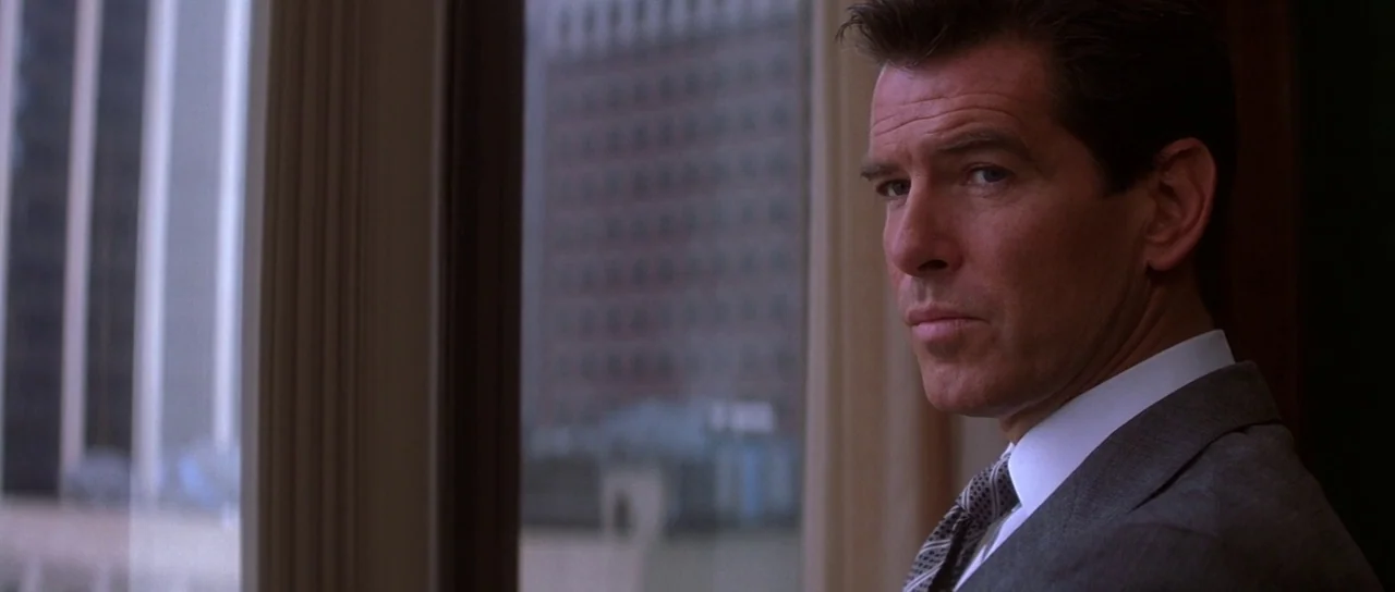 The Thomas Crown Affair (1999) movie still: medium — A man in a suit looks out a high window at city skyscrapers. The professional workspace is…