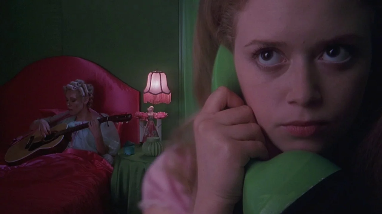 But I’m A Cheerleader (1999) movie still: closeup — A green-walled bedroom features a prominent pink satin bed and a vintage bedside lamp. A woman…