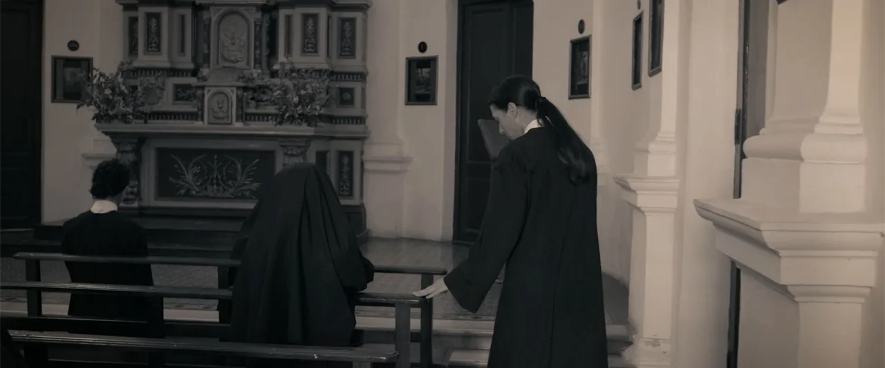 I Trust in You (2016) movie still: medium — The interior of a church features an altar in the background and wooden pews. A woman in a black robe…
