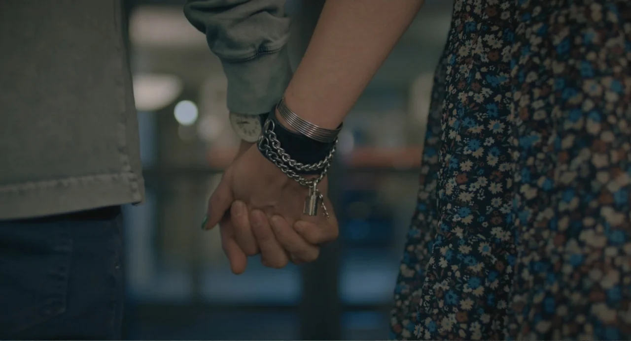The Map of Tiny Perfect Things (2021) movie still: closeup — A close-up view focuses on two people holding hands in an indoor space. The male wears…