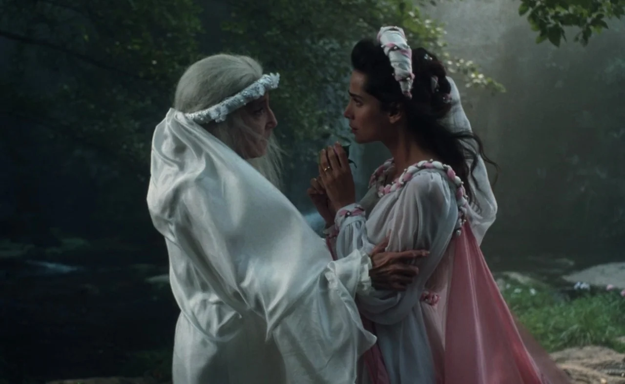 The Pit and The Pendulum (1991) movie still: medium — Two women stand in a misty, shaded woodland area with dense green foliage. One older woman…