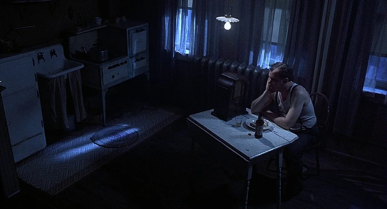 Chicago (2002) movie still: wide — A dark 1940s room features a vintage table, a radio, and a stove. A man sits by the table resting his head on his…