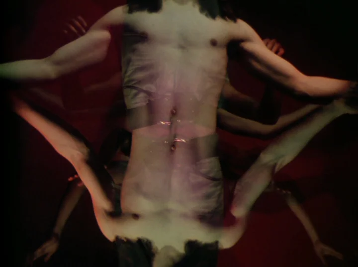 Invocation of My Demon Brother (1969) movie still: medium — A dark space features two superimposed figures mirrored vertically against a deep red…