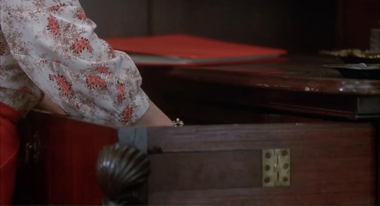 Teen Witch (1989) movie still: closeup — An open wooden desk drawer sits in a domestic interior setting. A woman's arm wearing a floral blouse…