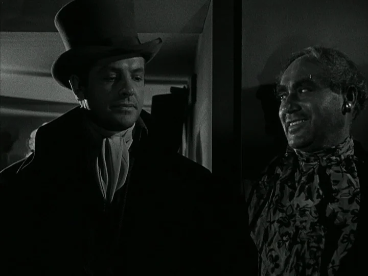 The Black Book (Reign of Terror) (1949) movie still: medium — A dimly lit indoor passage featuring two men engaged in a close encounter. The man on…