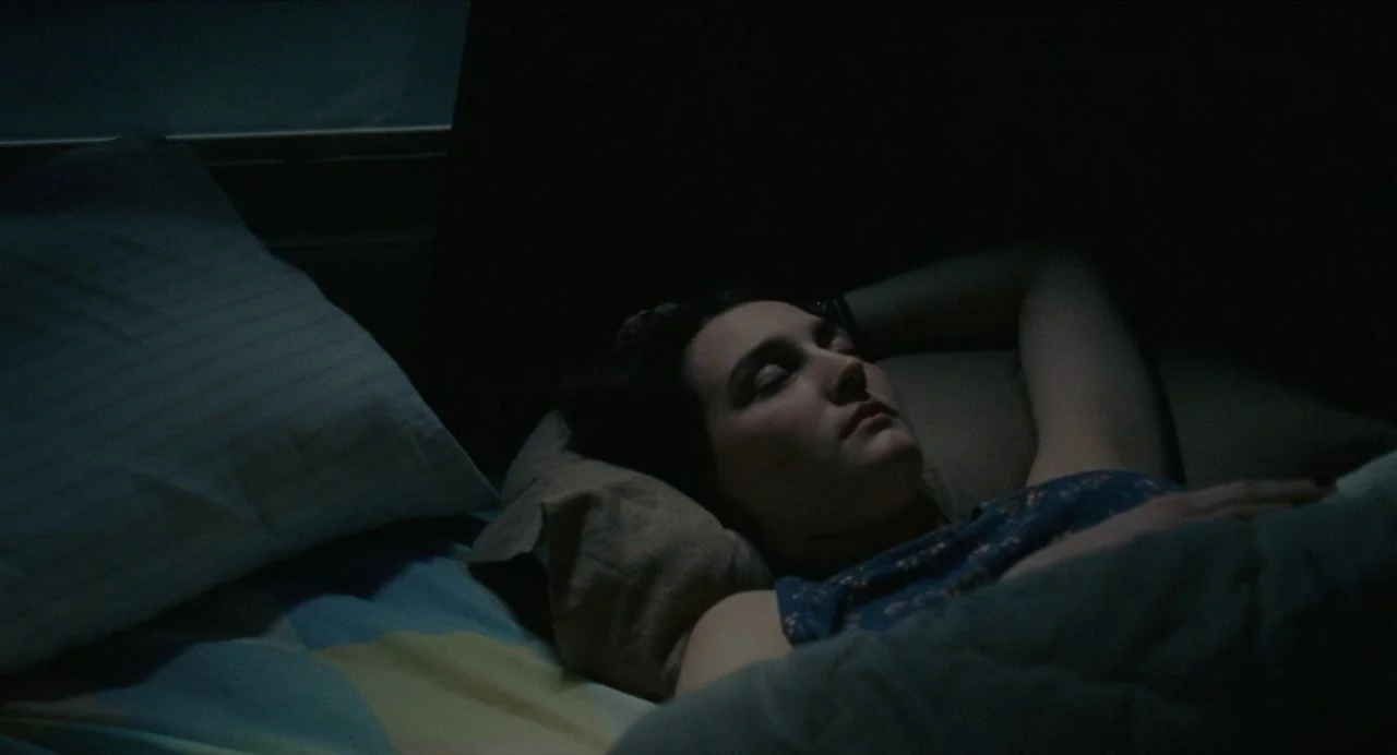 Never Rarely Sometimes Always (2020) movie still: closeup — A dark, dimly lit bedroom at night with a person sleeping in a bed. The person lies on a…
