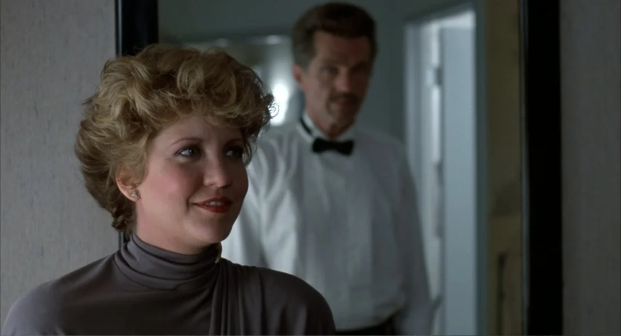 Poltergeist III (1988) movie still: medium — An interior space features a foreground woman in focus and a blurred man standing behind. The woman…