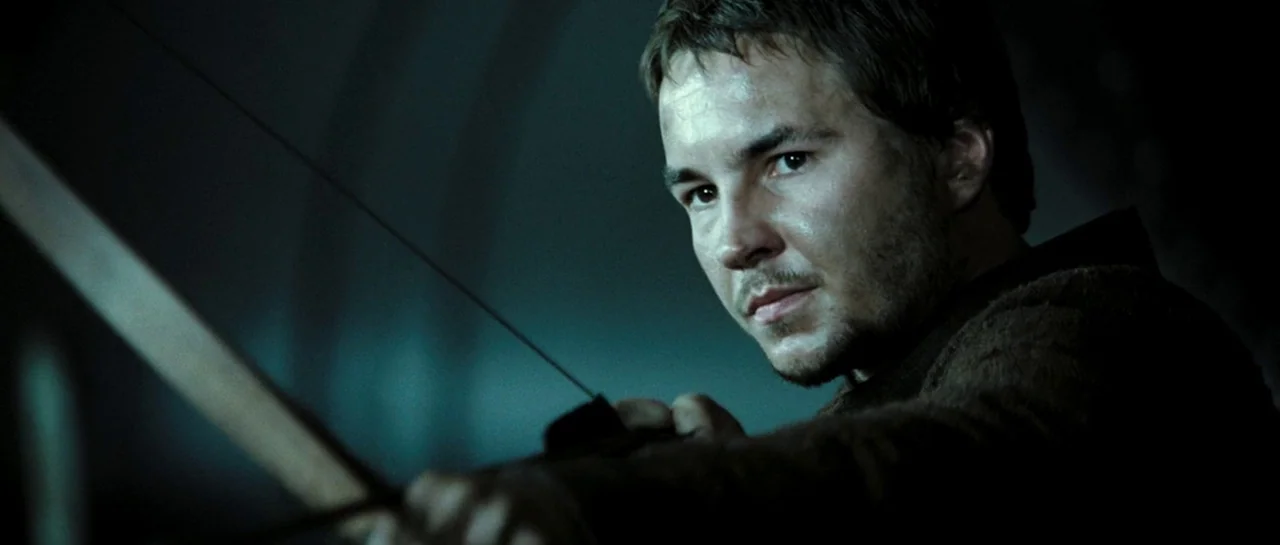 Doomsday (2008) movie still: closeup — A dark, dimly lit environment with out-of-focus background textures suggesting a vast space. A man pulls back…