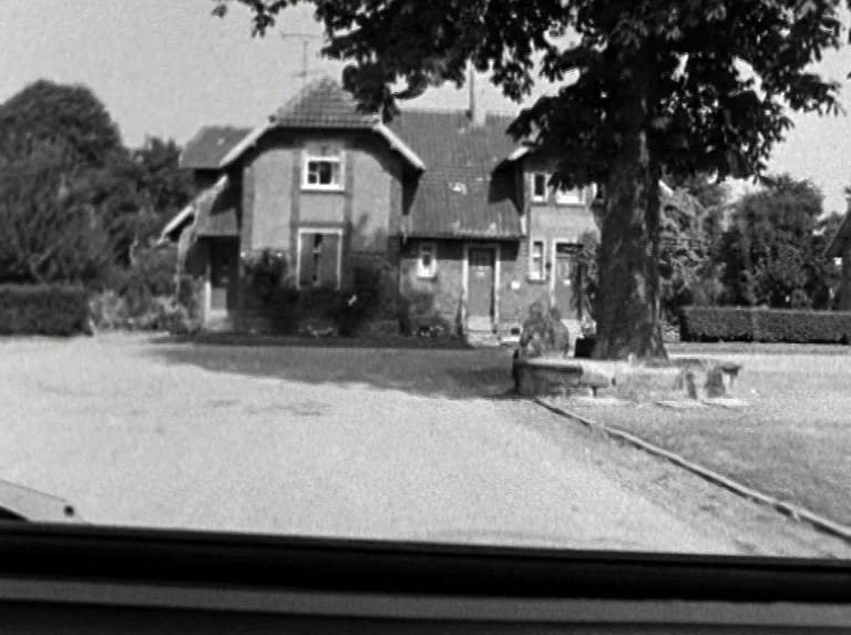 Alice in the Cities (1974) movie still: establishing — A traditional multi-story residential building with a tiled roof stands among green foliage.…