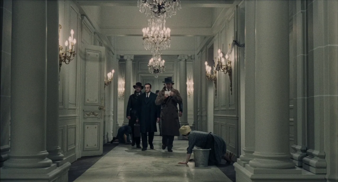 The Army of Shadows (1969) movie still: wide — An opulent, long corridor in an old hotel features white columns and multiple chandeliers. Three men…