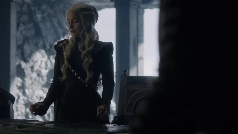 Game of Thrones (2017) movie still: medium — A dark stone hall features large arched pillars backlit by daylight. A woman stands at a table looking…