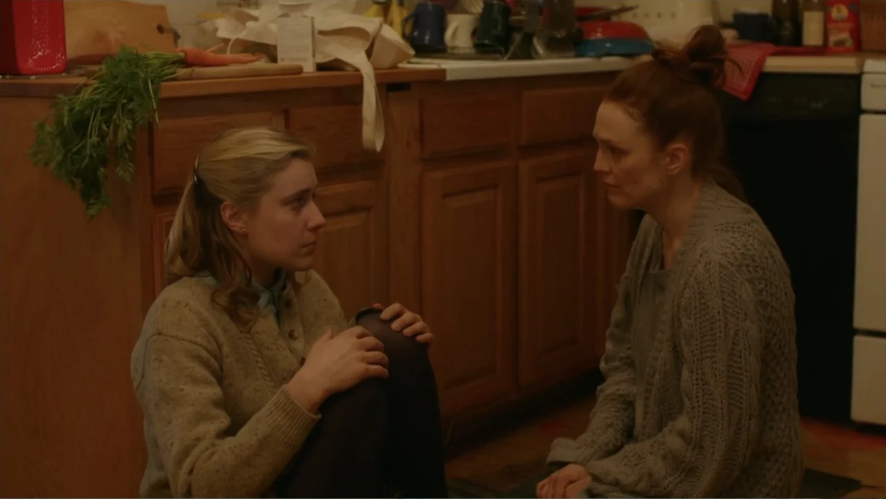 Maggie's Plan (2016) movie still: medium — A cluttered residential kitchen with wooden cabinets and a countertop featuring produce and clutter. Two…