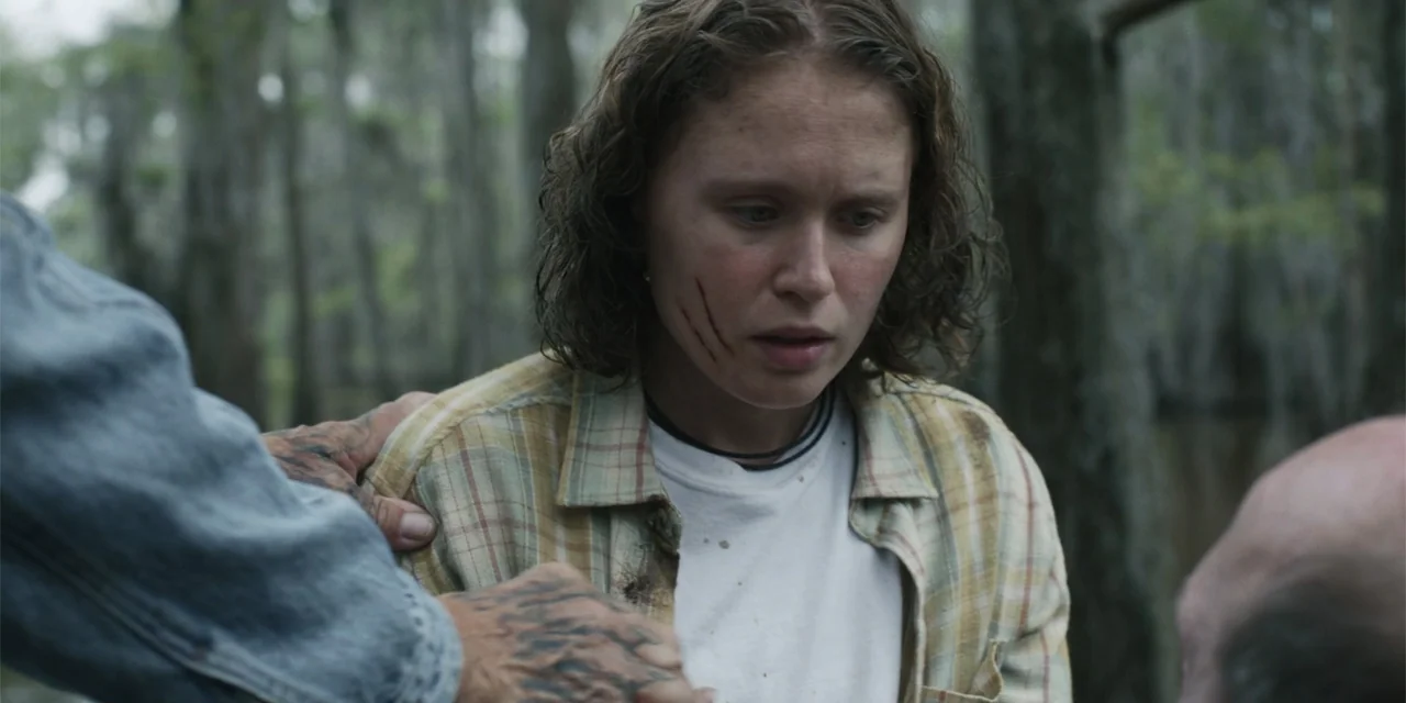Caddo Lake (2024) movie still: medium — A swamp with blurred cypress trees and murky water occupies the background. A tattooed hand touches a…