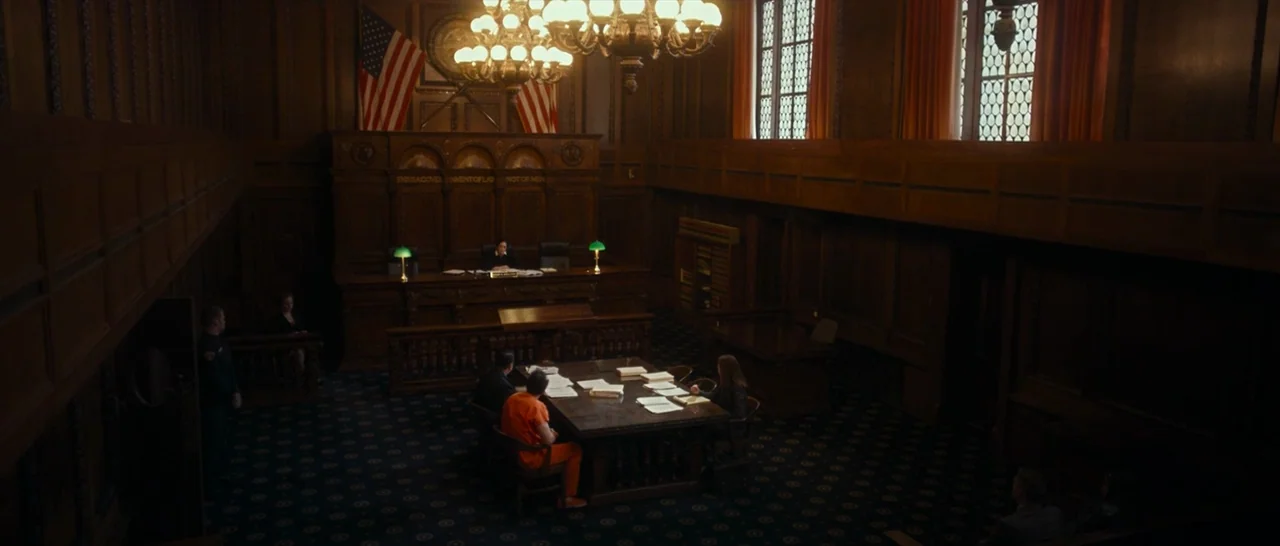 Dog Eat Dog (2016) movie still: wide — A spacious wood-paneled room has a judge's bench and a central table with documents. A person in an orange…