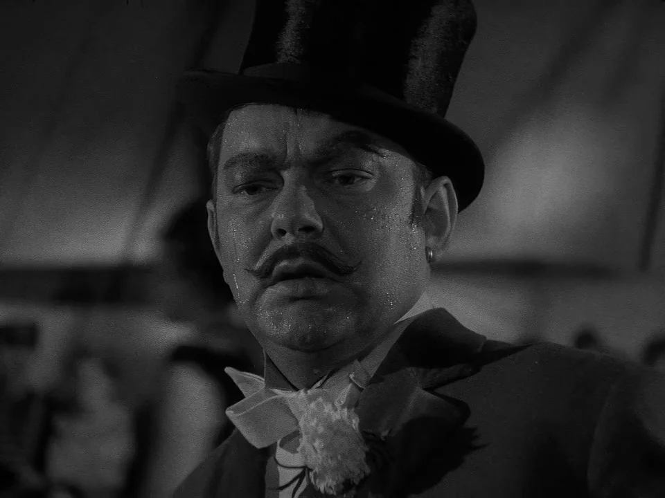 Sawdust and Tinsel (1953) movie still: closeup — A man in formal attire sits inside a canvas tent under dim lighting conditions. The subject…