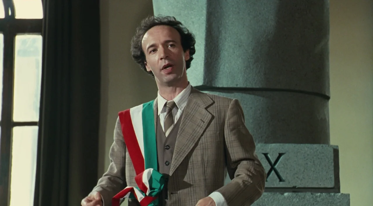 Life is Beautiful (1997) movie still: medium — A formal government room features a large stone column and a tall window. A man in a suit and a…