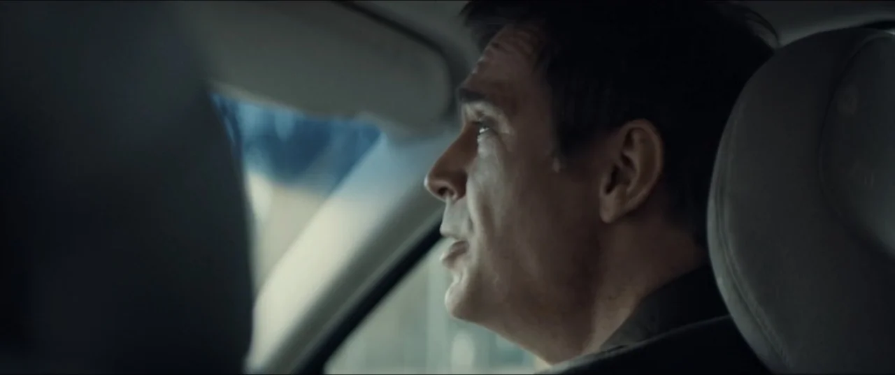 Bonus Track (2024) movie still: closeup — A view inside a car cabin focusing on the driver from behind the passenger seat. The man in the driver…