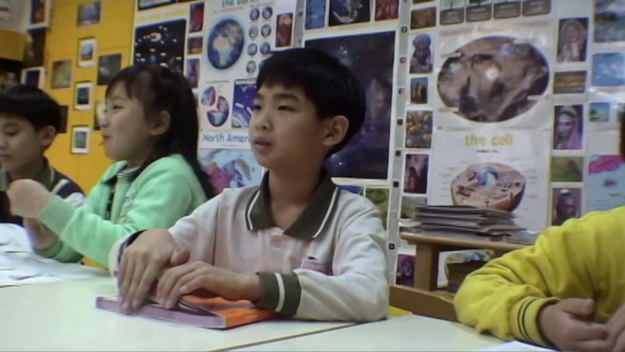 Daniel (1983) movie still: medium — A classroom features educational posters and charts attached to the yellow back wall. Three students sit at…