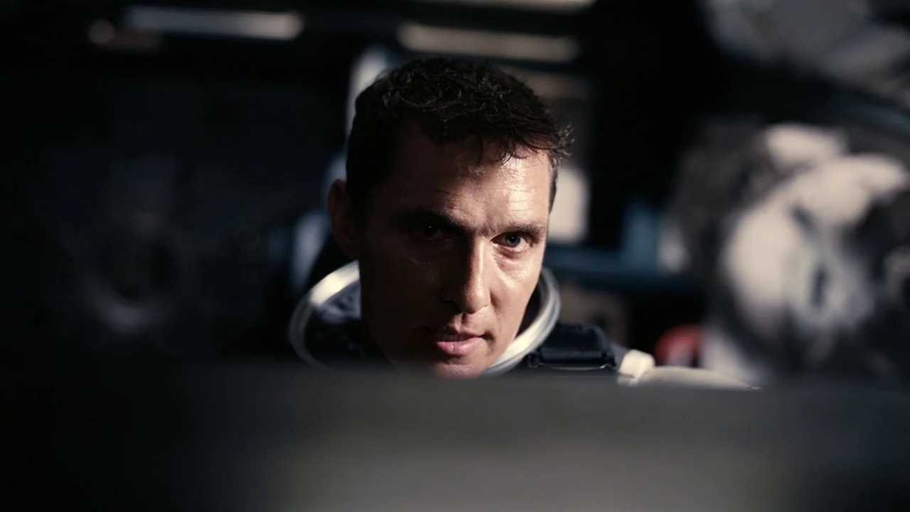 Interstellar (2014) movie still: closeup — A dark, cramped environment inside a futuristic cockpit with metallic surfaces. A man in a space suit…