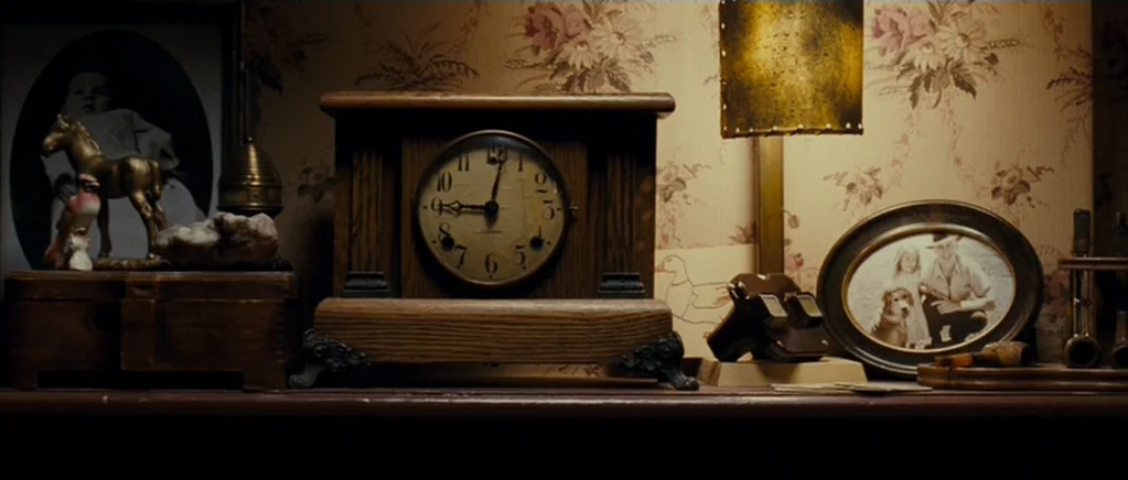 Paul (2011) movie still: closeup — A wooden mantelpiece features a vintage clock and framed family photographs against floral wallpaper. These items…