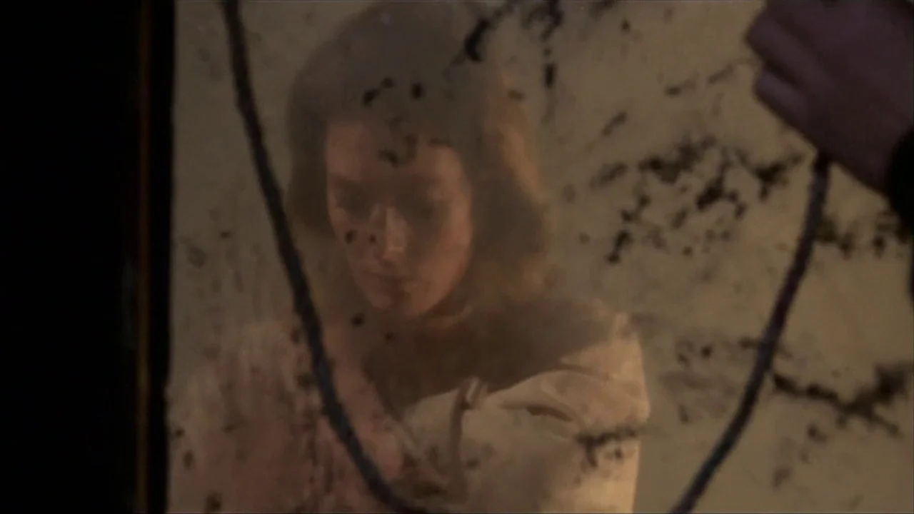 A Quiet Place In The Country (1968) movie still: closeup — A woman looks into a damaged, grime-streaked mirror in a dim room. She is positioned…