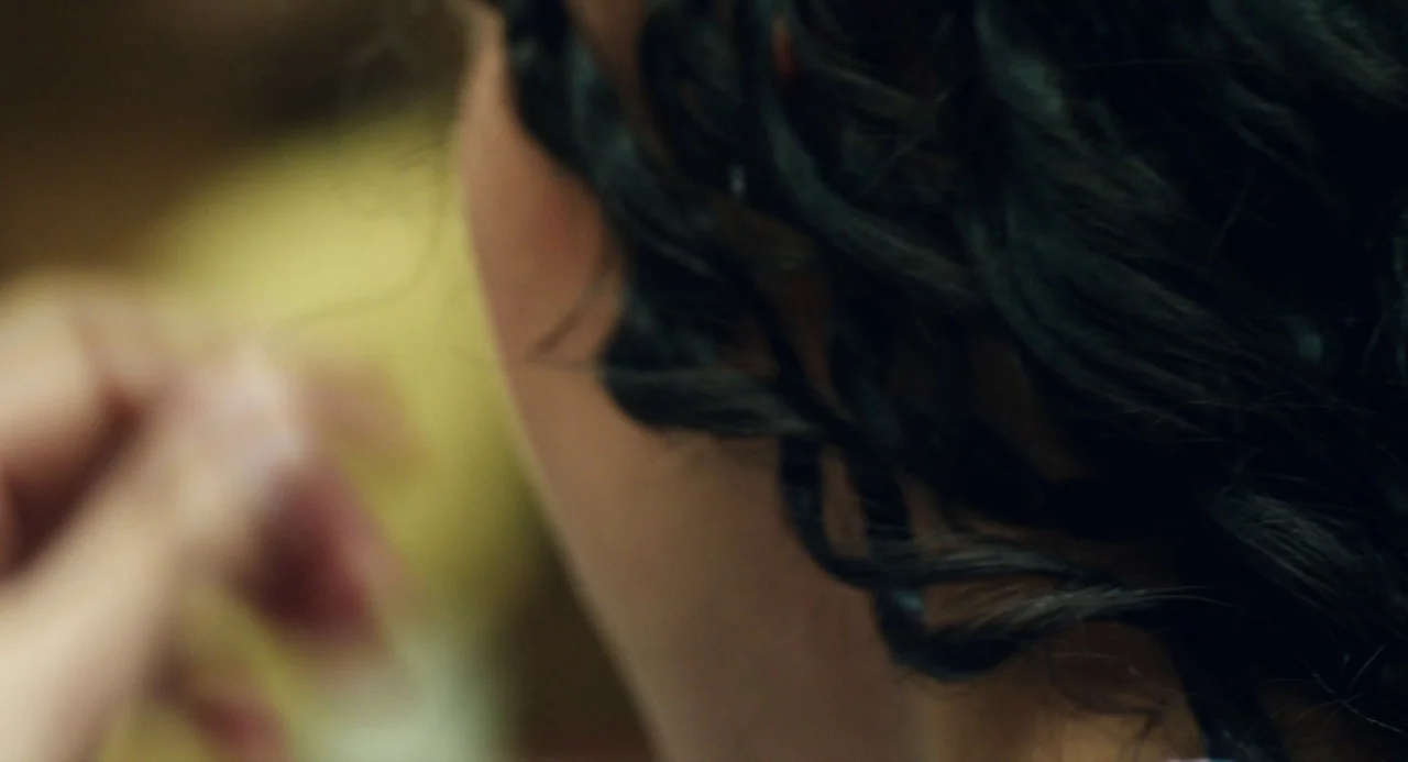 The Miseducation of Cameron Post (2018) movie still: closeup — A dark-haired person is partially seen from behind in an indeterminate indoor…