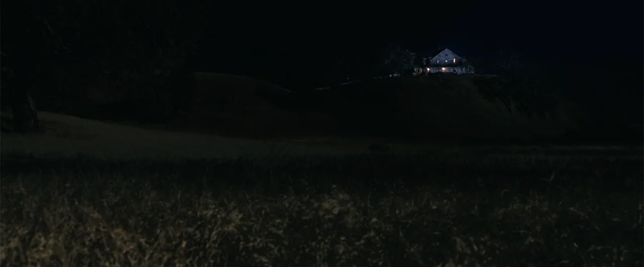Annabelle: Creation (2017) movie still: establishing — A dark, grassy field sits beneath a night sky with a house atop a hill. The house is…