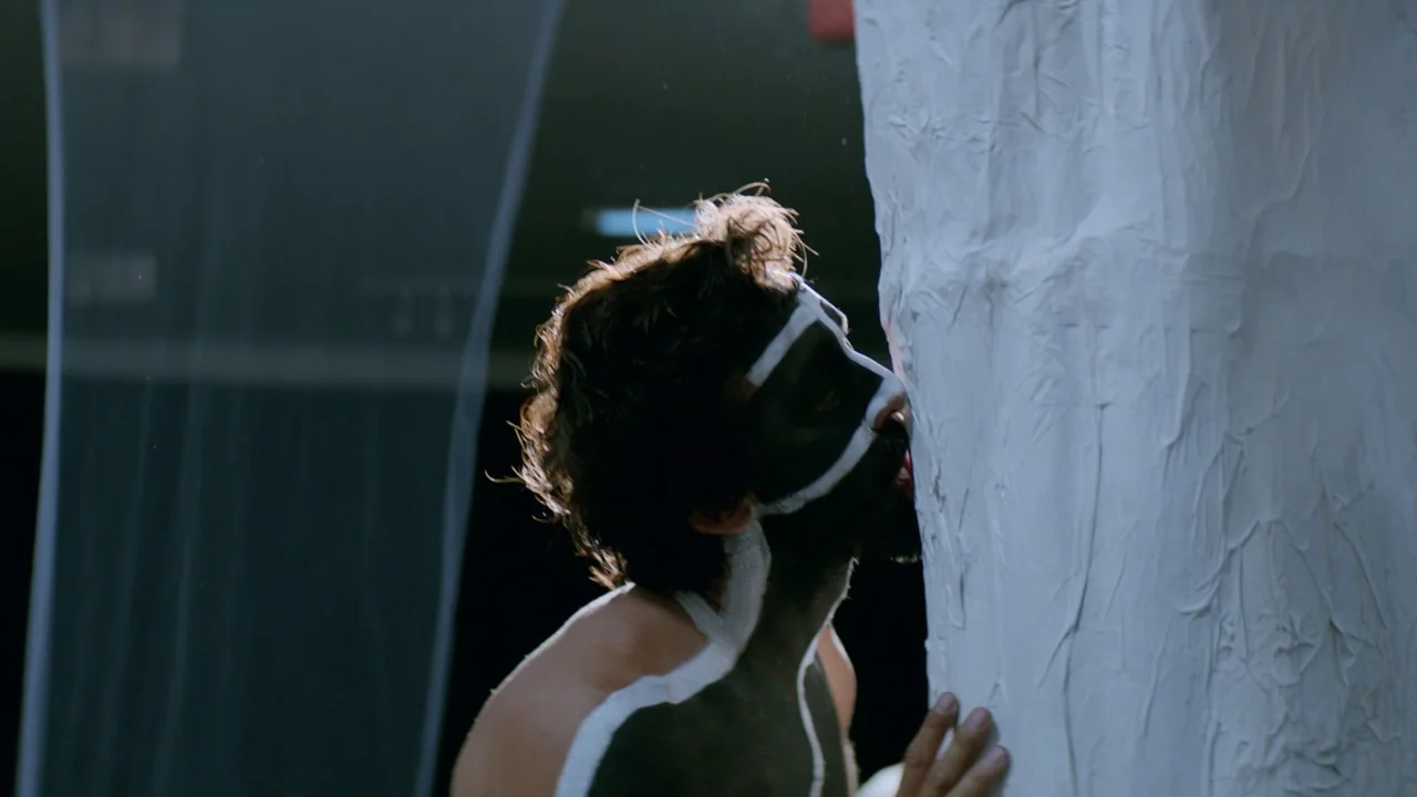That's Not Cheating (2016) movie still: medium — A dark studio environment features a vertical white textured pillar against a black backdrop. A…