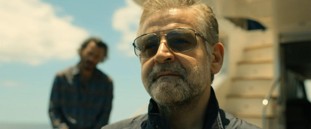 Den of Thieves 2: Pantera (2025) movie still: closeup — A sunny outdoor yacht deck features a man in the foreground and another figure. The man in…