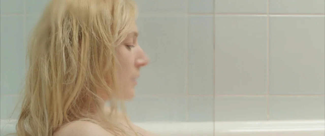 On Body and Soul (2017) movie still: closeup — A light blue tiled enclosure surrounds the space where the subject is positioned. A woman with blonde…