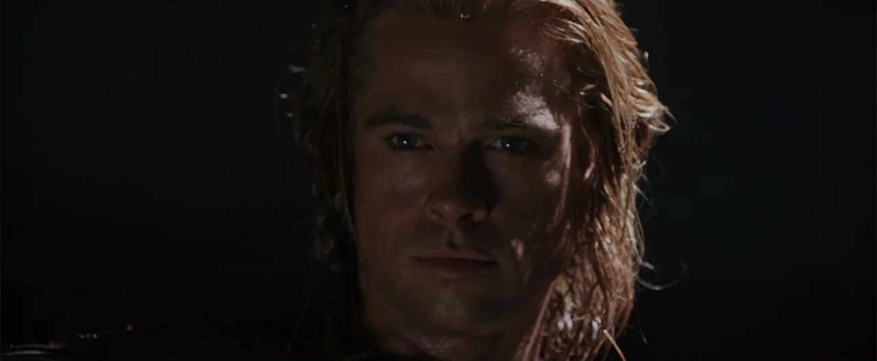 Troy (2004) movie still: closeup — A man stands in darkness against an obscured background at night. The man stares forward with illuminated facial…