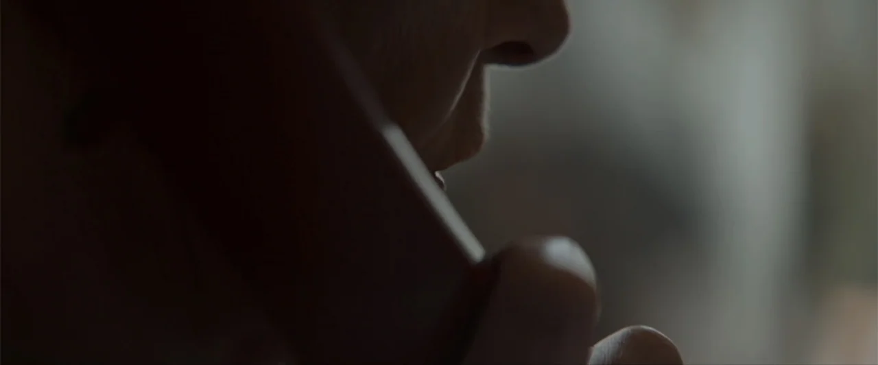 La herencia (2010) movie still: closeup — A dimly lit indoor space featuring the lower profile of a person. A person holds a telephone receiver…