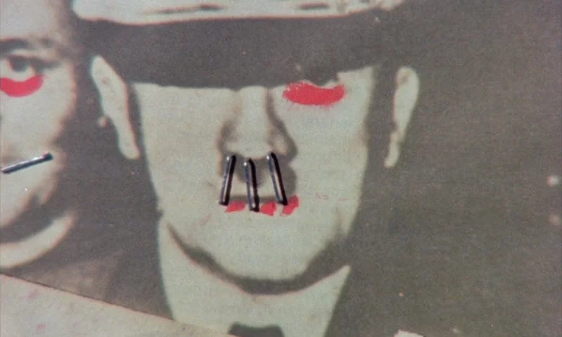 Jubilee (1978) movie still: closeup — A vintage black and white photograph lies on a surface. The portrait face is marked with red paint and…