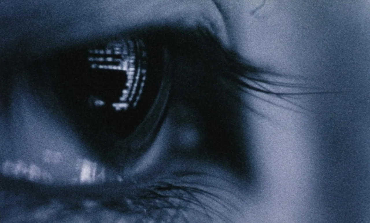 Evil Dead Trap (1988) movie still: closeup — An extreme close-up of a human eye captured with high contrast and visible grain. A bright grid-like…
