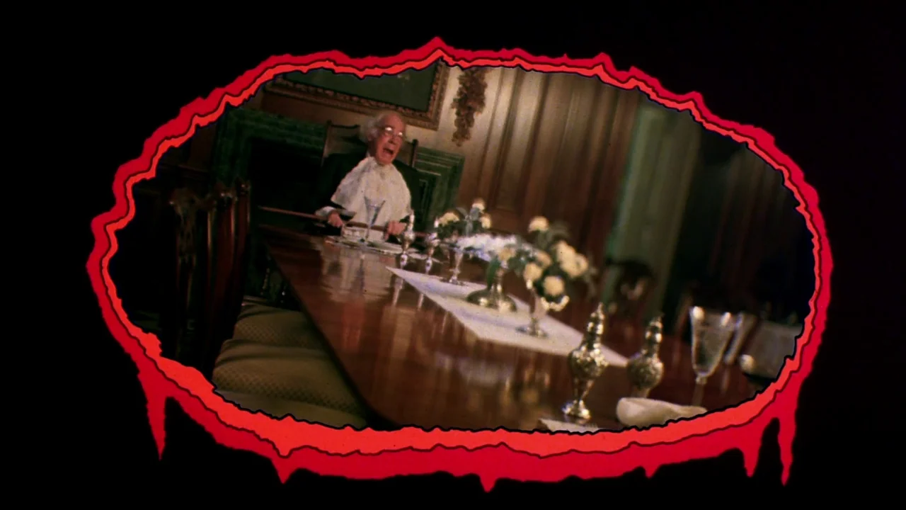 Creepshow (1982) movie still: wide — An elderly man yells from the head of a formal wood-paneled dining room. The entire frame is contained within a…