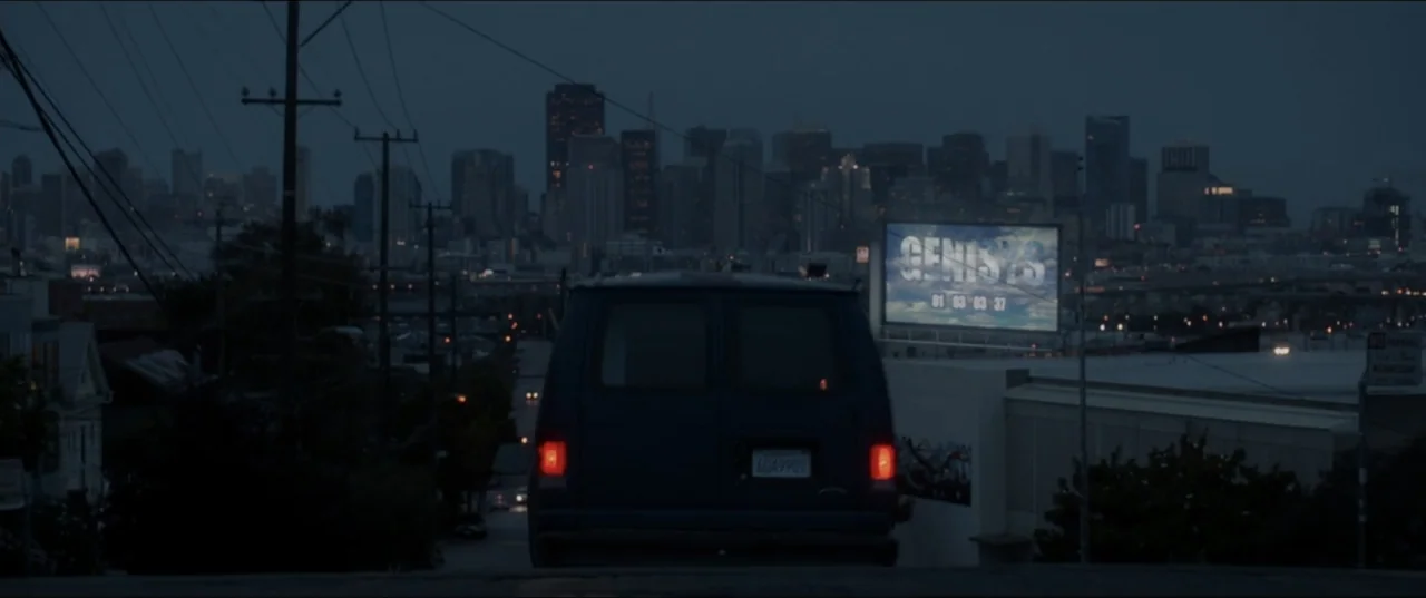 Terminator Genisys (2015) movie still: wide — A dark van sits on an incline overlooking a distant urban city skyline. A large billboard with text is…