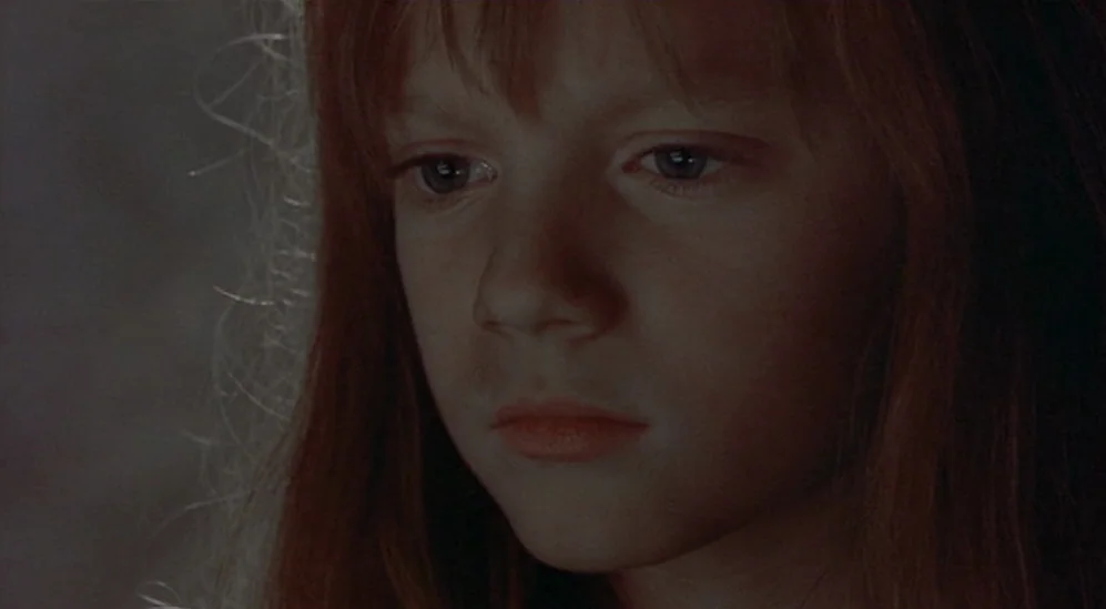 The Adventures Of Baron Munchausen (1988) movie still: closeup — A dark, undifferentiated interior space frames a young girl with auburn hair. The…